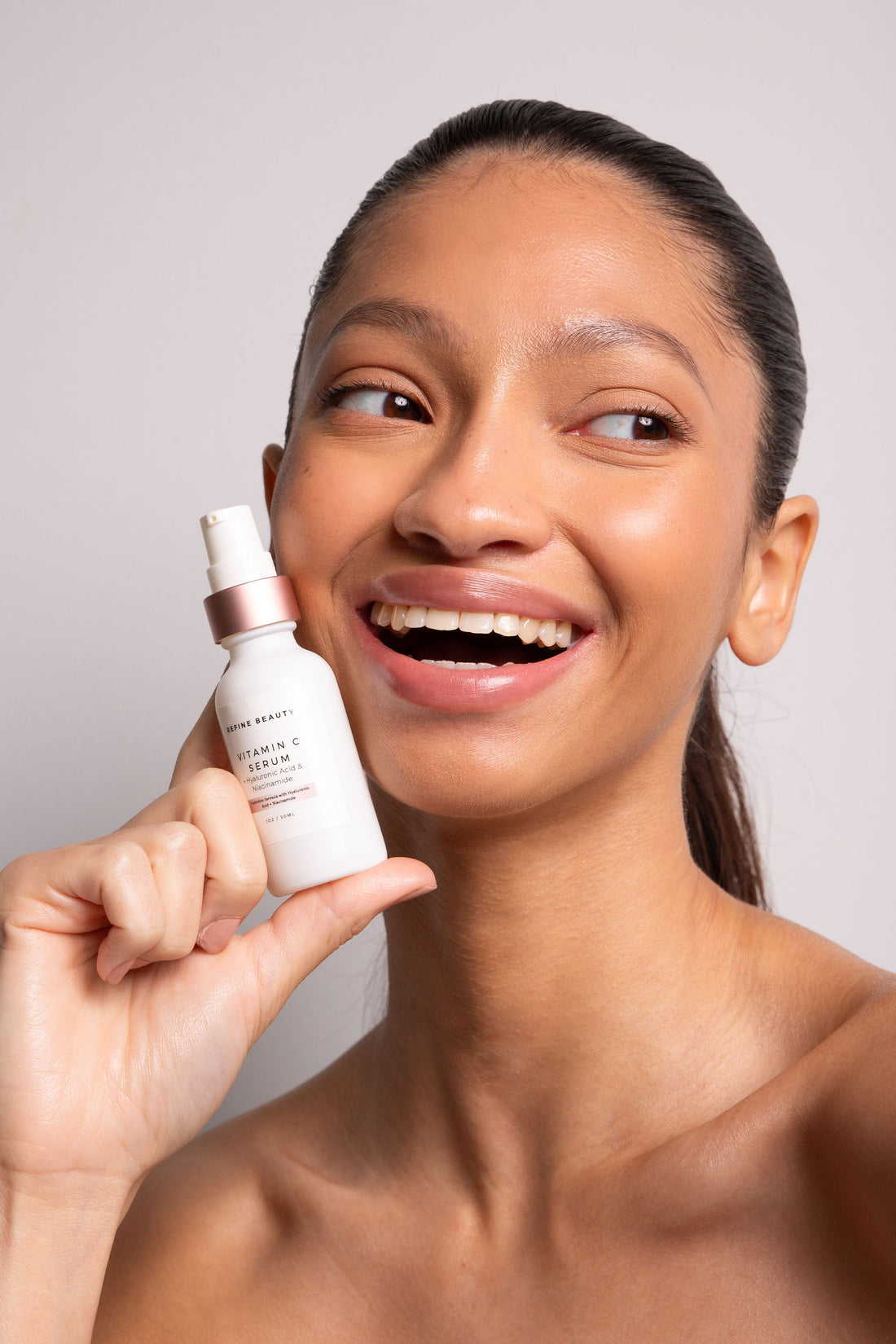 Model holding a Vitamin C Serum with Hyaluronic Acid + Niacinamide on white background 