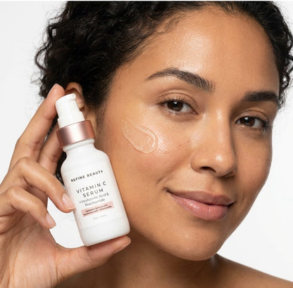 Woman holding a Refine Beauty Vitamin C Serum  with visible product on her face.