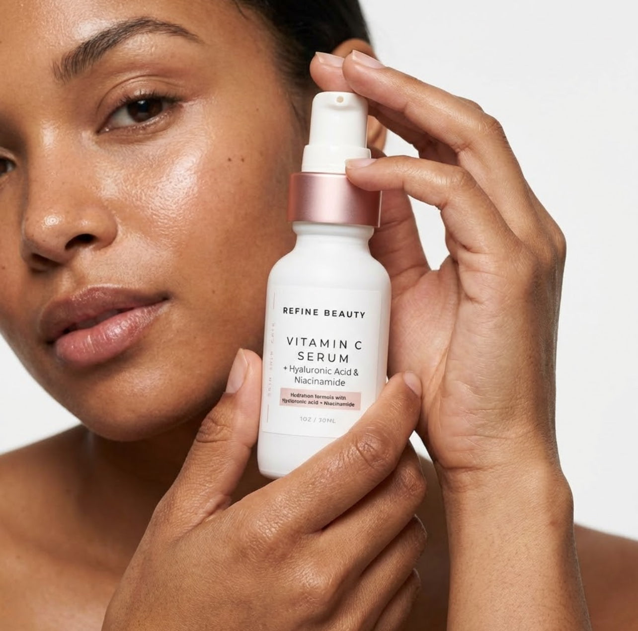 Woman holding a bottle of Refine Beauty Vitamin C Serum against a neutral background
