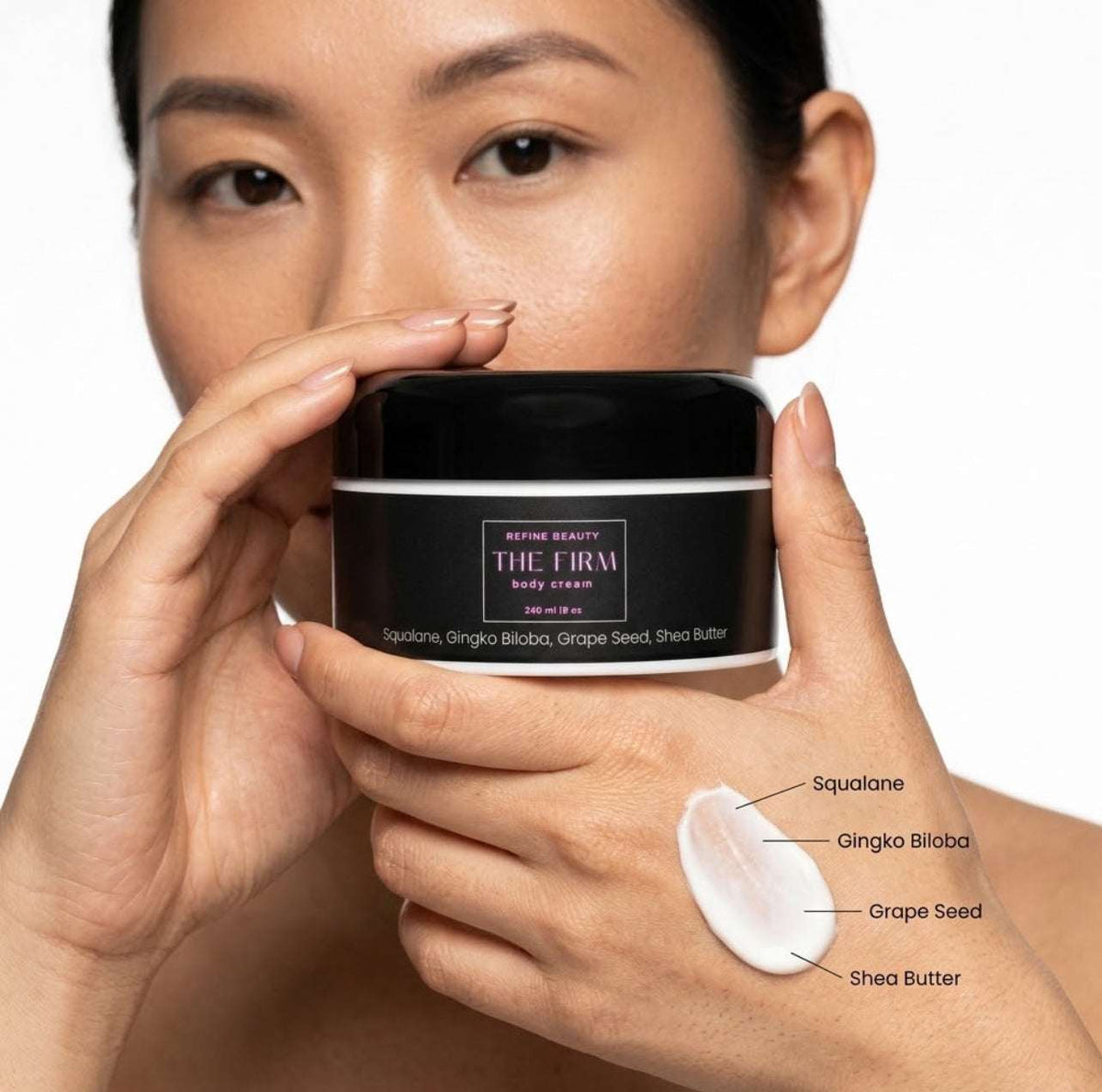 A woman holds a black jar of Refine Beauty The Firm Body Cream against a white background, with a swatch of the white cream shown on her hand and ingredient labels pointing to Squalane, Gingko Biloba, Grape Seed, and Shea Butter.