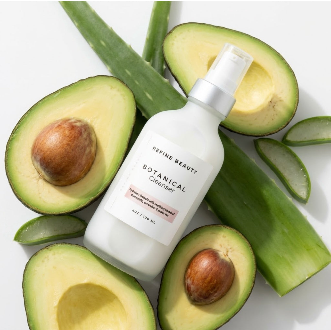 Skincare bottle labeled Refine Beauty Botanical Cleanser surrounded by sliced avocados on a white background