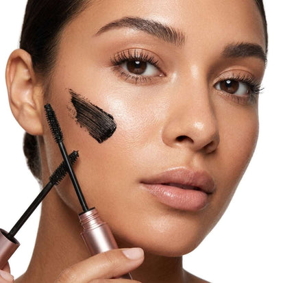 Woman applying Refine Beauty volume mascara  to her eyelashes with a brush on a white background