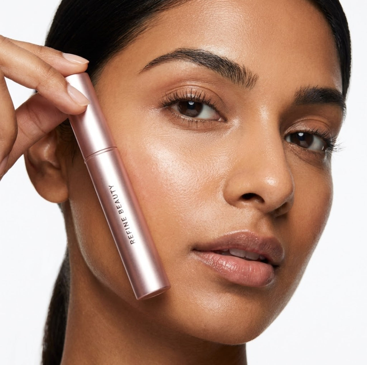 Woman applying makeup with a pink Refine Beauty volume mascara on a neutral background