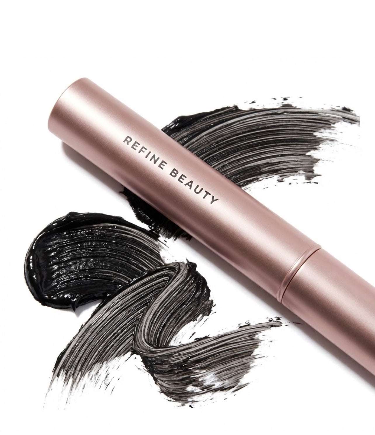 Rose gold  Refine Beauty Volume mascara with black smudges on a white background