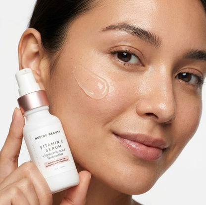 Woman applying Refine Beauty vitamin C serum to her face with a close-up of the product.
