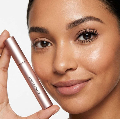 Woman holding a pink makeup product with Refine Beauty volume mascara  against a neutral background