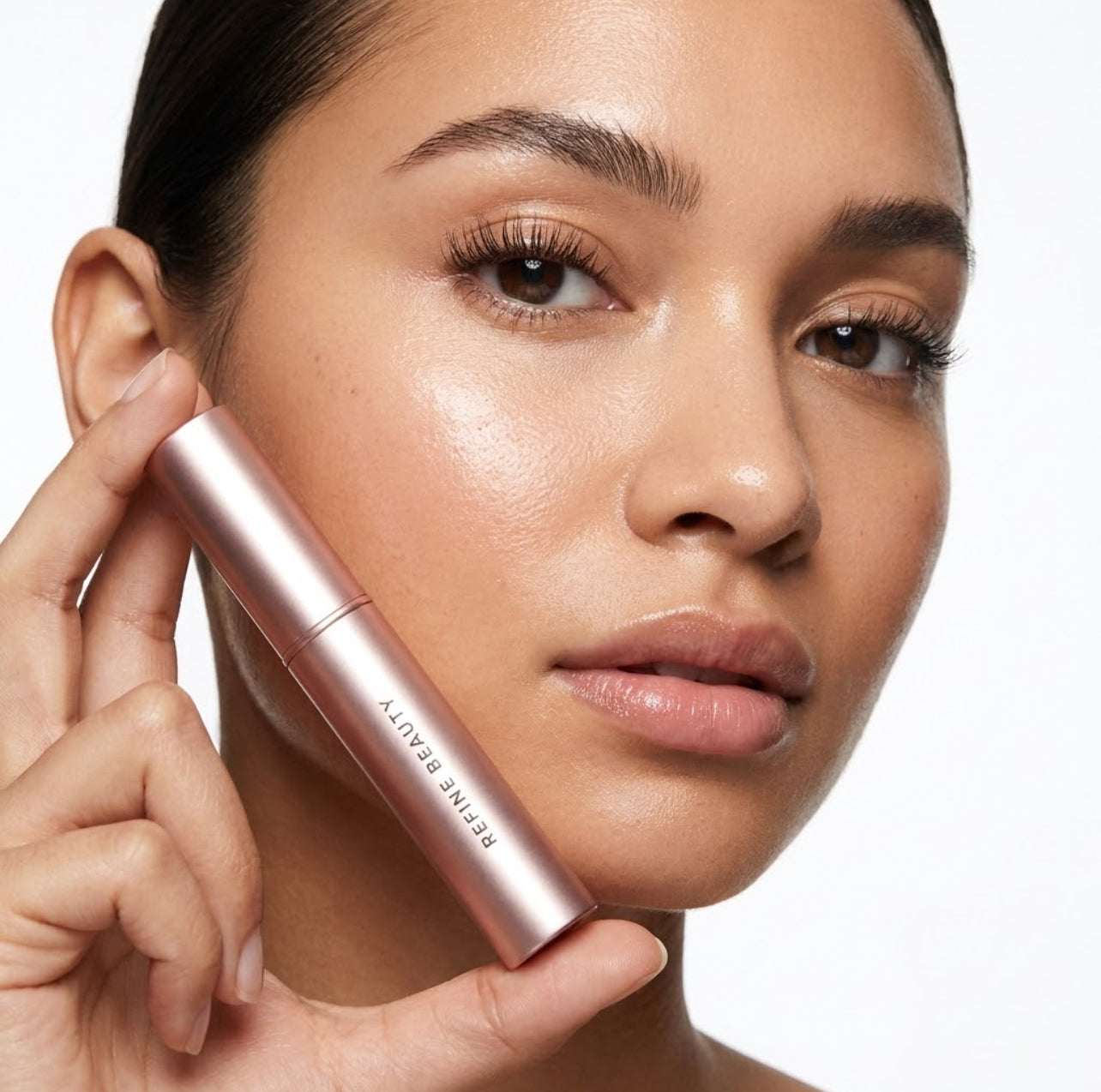 Woman holding Refine Beauty volume mascara close to her face on a white background