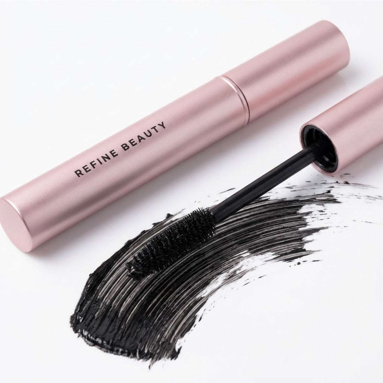 Refine Beauty Volume Mascara with black bristle brush and pink tube on a white background