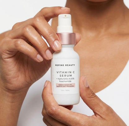 Hand holding a bottle of Refine Beauty Vitamin C Serum with a blurred background