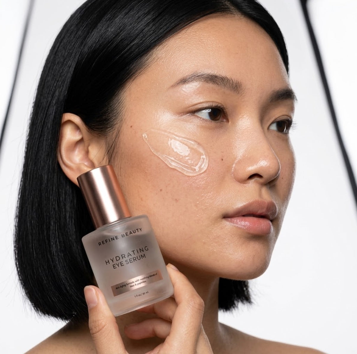 Model holding Refine Beauty Hydrating Eye Serum with clear gel swatch on white background 