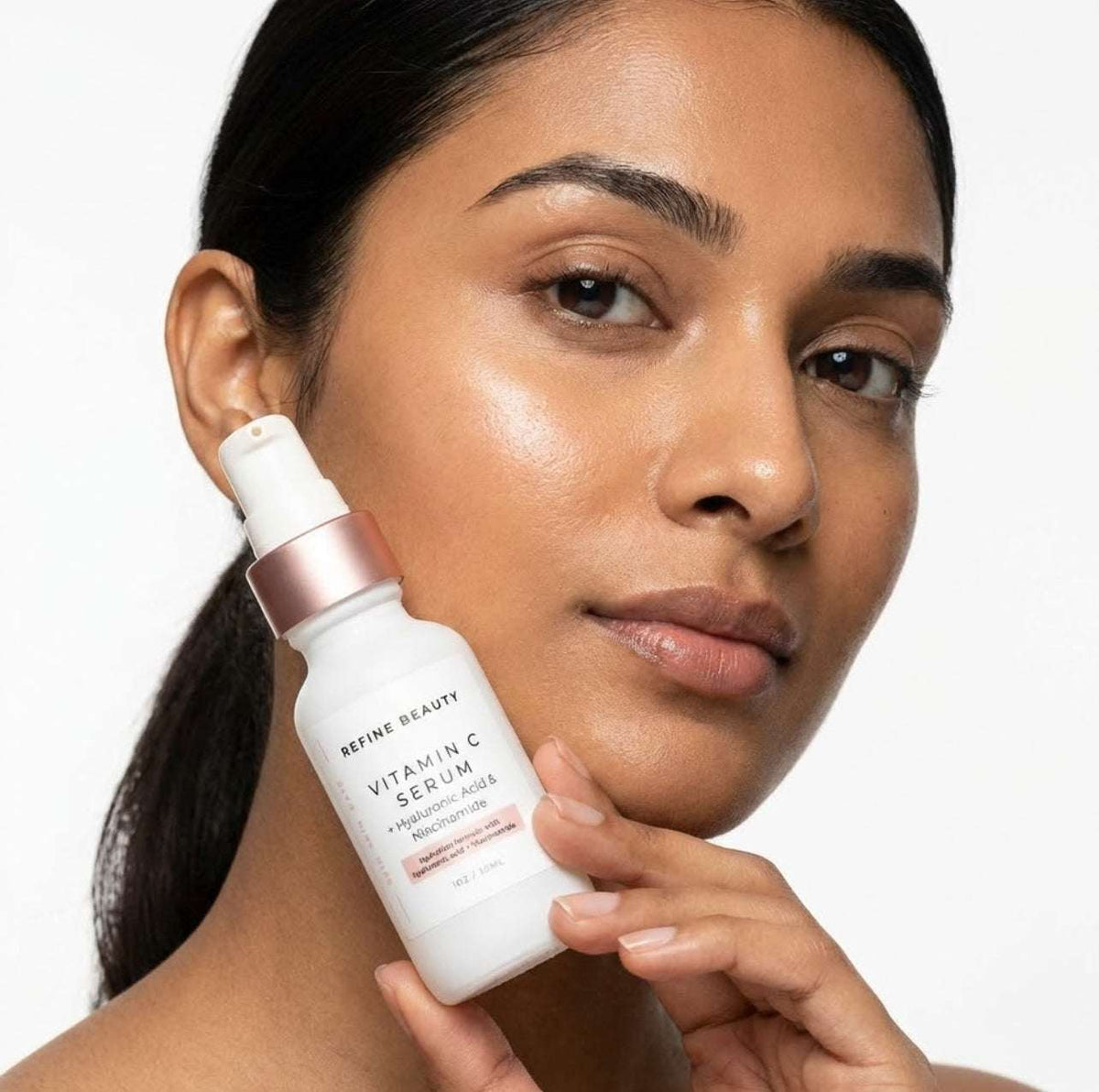 Woman holding a Refine Beauty Vitamin C serum bottle with a neutral background